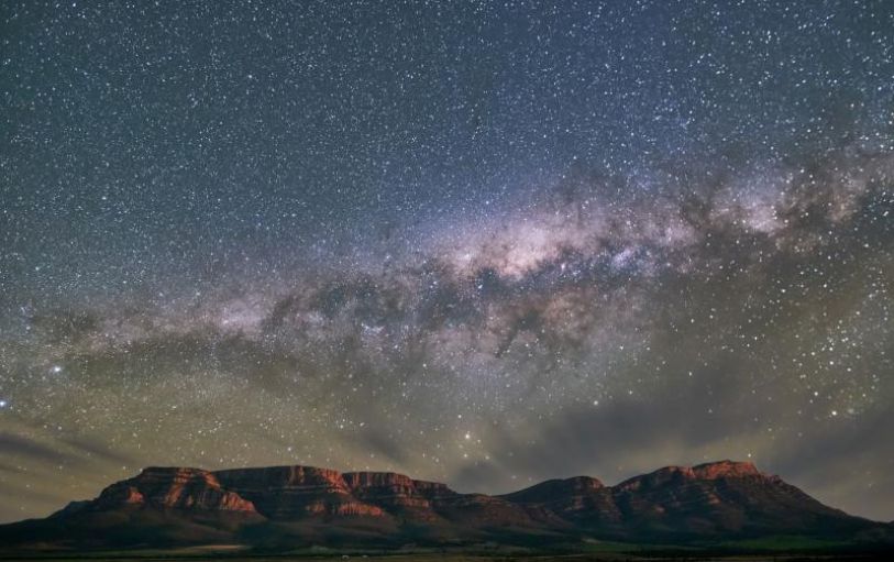 A girl with blonde hair in a black tshirt looking at sunset over an empty valley  in the Australian Outback on the 8 day Adelaide to Uluru adventure