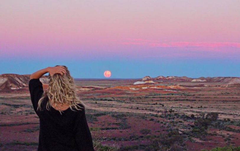 A girl with blonde hair in a black tshirt looking at sunset over an empty valley  in the Australian Outback on the 8 day Adelaide to Uluru adventure