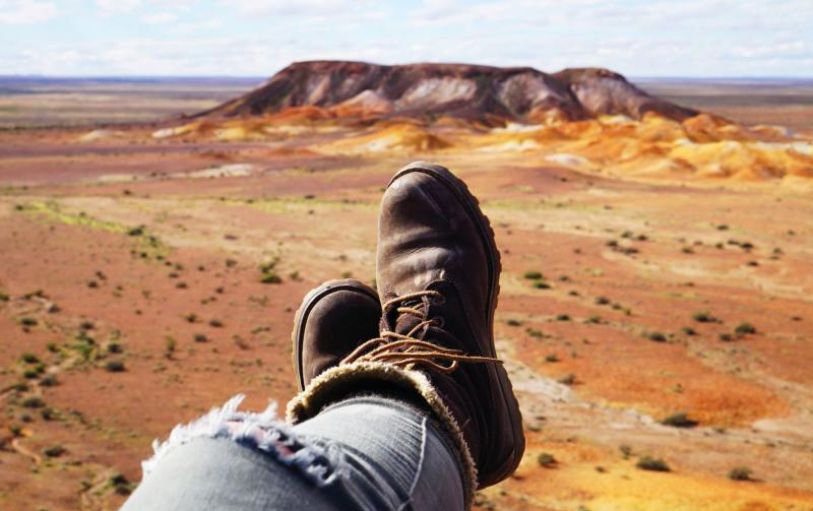 A girl with blonde hair in a black tshirt looking at sunset over an empty valley  in the Australian Outback on the 8 day Adelaide to Uluru adventure