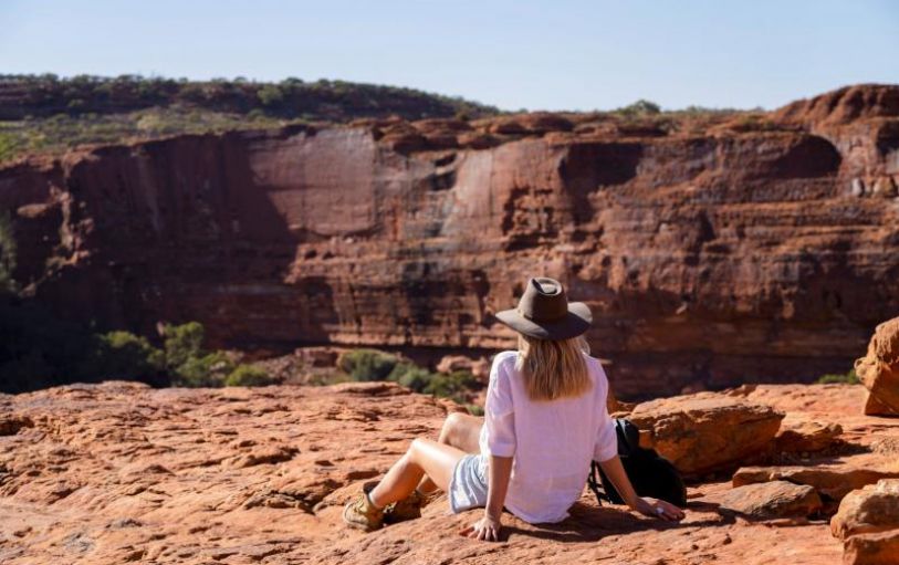 A girl with blonde hair in a black tshirt looking at sunset over an empty valley  in the Australian Outback on the 8 day Adelaide to Uluru adventure
