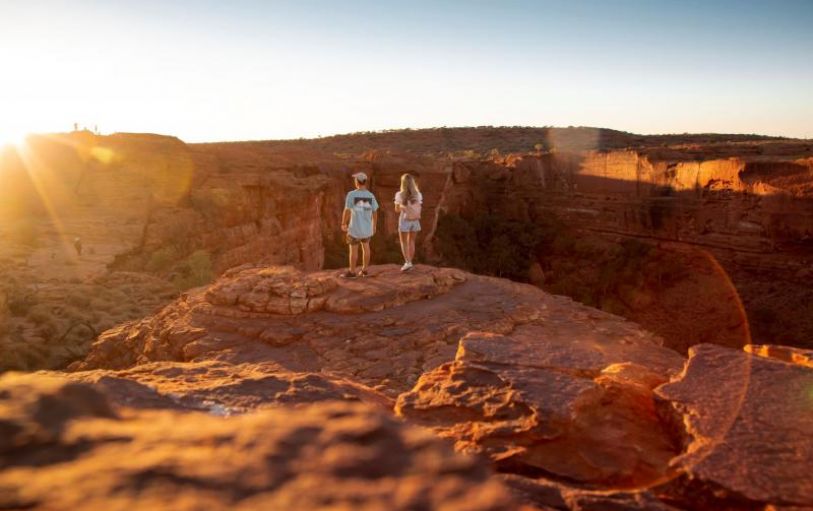 A girl with blonde hair in a black tshirt looking at sunset over an empty valley  in the Australian Outback on the 8 day Adelaide to Uluru adventure