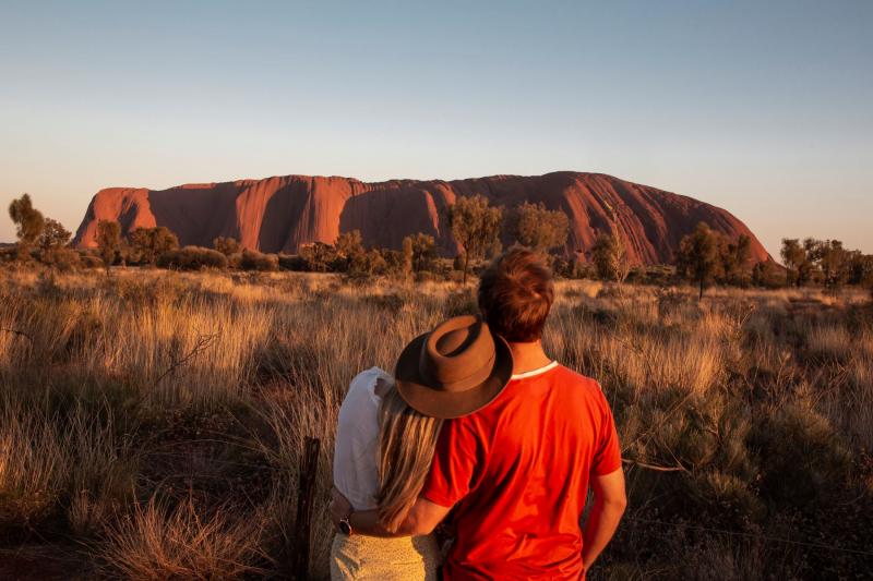 2 backpackers enjoying the view of Uluru during a sunset on the 7 day Uluru to Adelaide experience