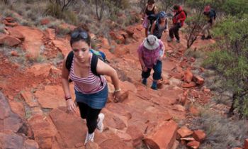 Six Backpackers hiking the red mountainous landscape of Uluru Kata Tjuta and Kings Canyon during the 3 night Rock the centre tour