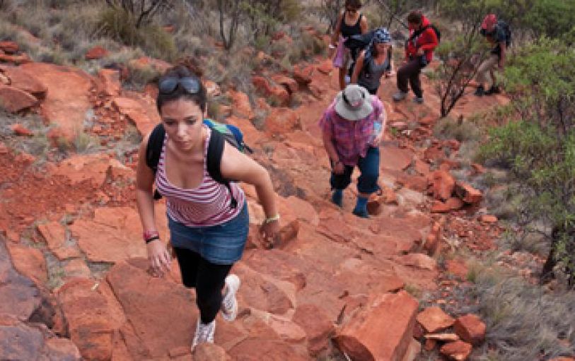 Six Backpackers hiking the red mountainous landscape of Uluru Kata Tjuta and Kings Canyon during the 3 night Rock the centre tour