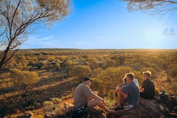 backpackers on a hill watching sunset over the red centre on a rock the centre trip