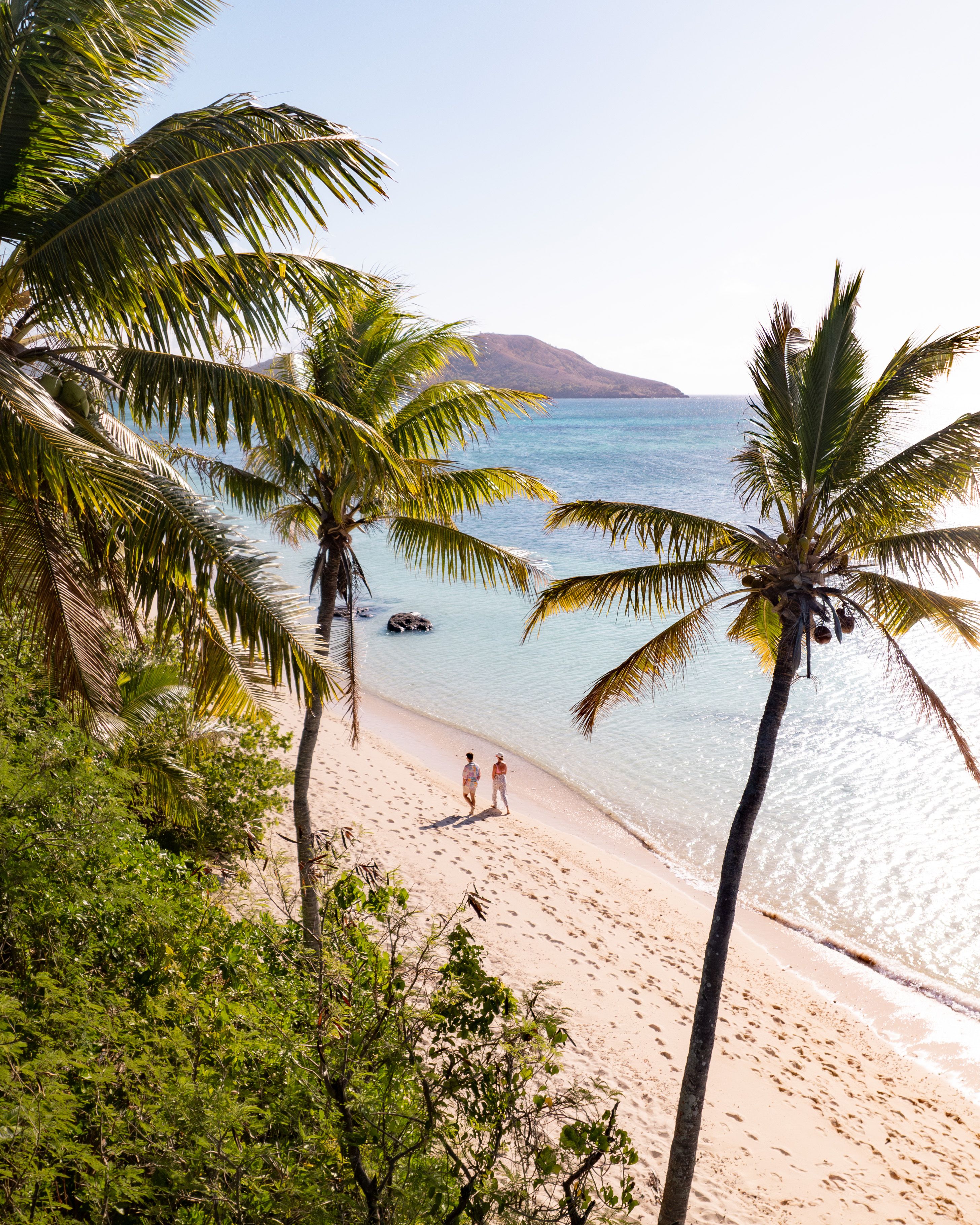 Couple walking along tropical beach in Fiji with crystal clear blue waters and palm trees