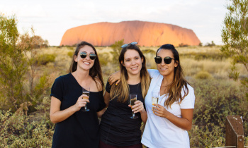 Three backpackers enjoying a glass of champagne at Uluru at sunset during the 3 Day Rock the Centre