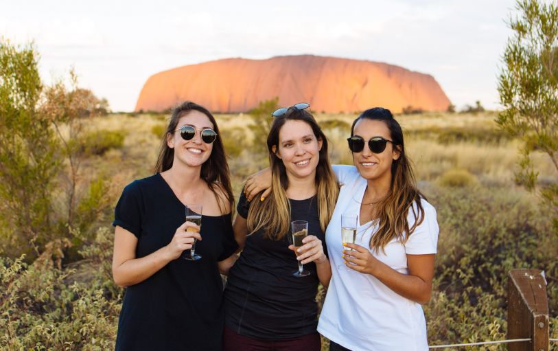 Three backpackers enjoying a glass of champagne at Uluru at sunset during the 3 Day Rock the Centre