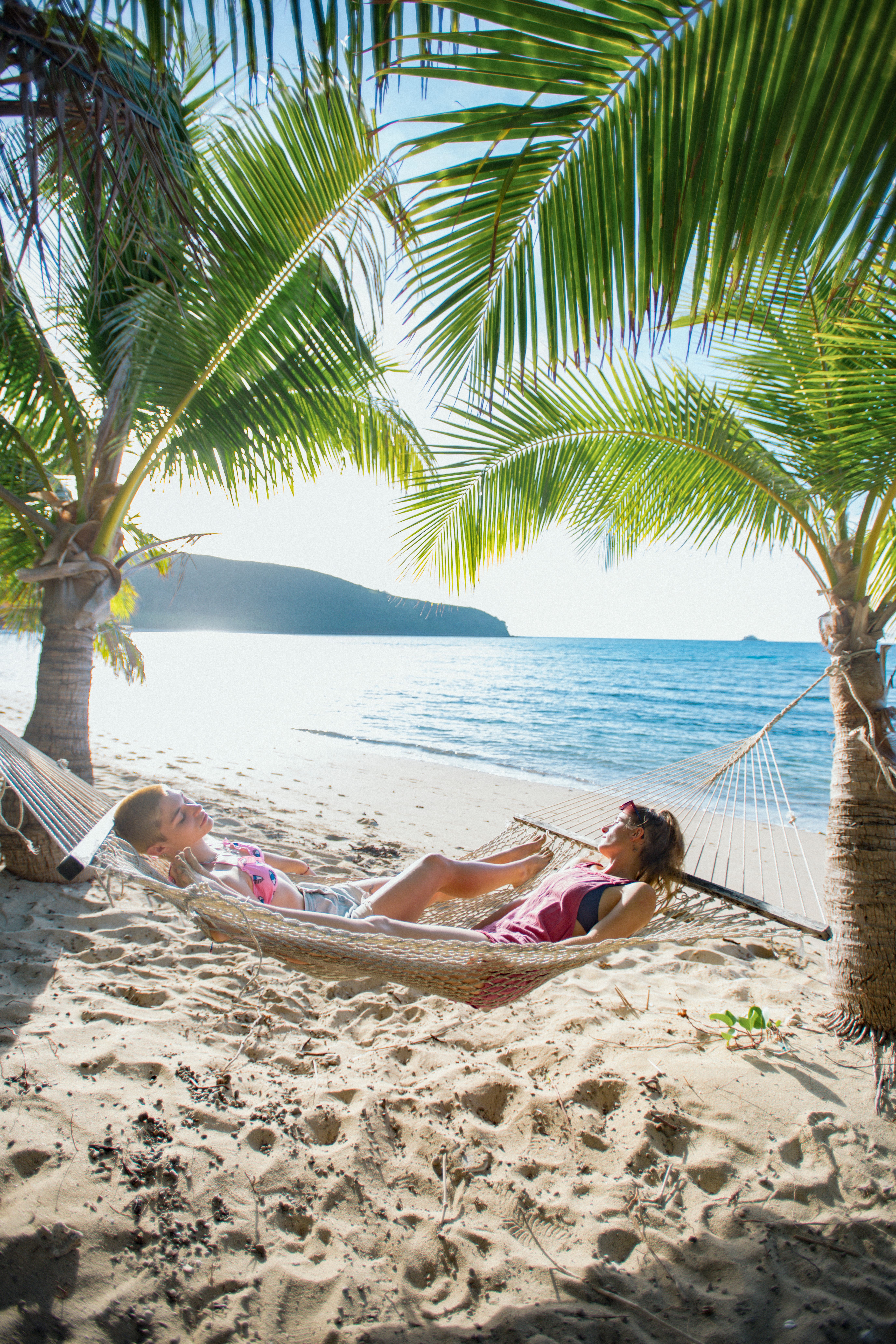 two people relaxing in a hammock on a tropical beach in Fiji with white sand blue sea and palm trees
